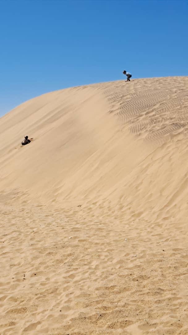 Adventurers climbing to the top of a massive sand dune in the Namib Desert