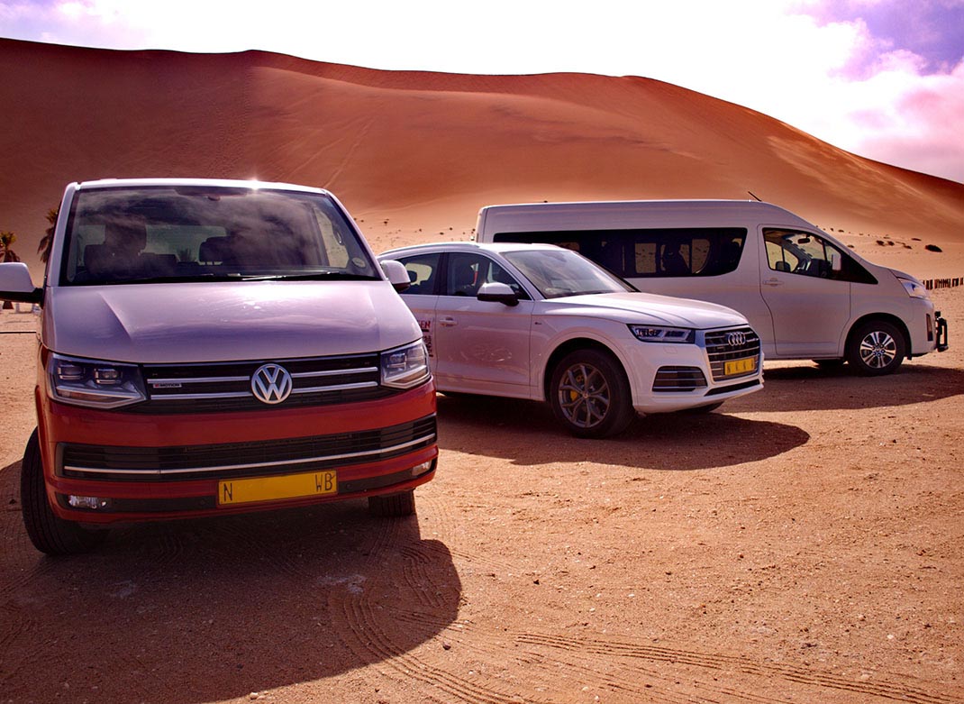 SEGEN Tours fleet including VW van, Audi SUV, and minibus parked at the desert dunes