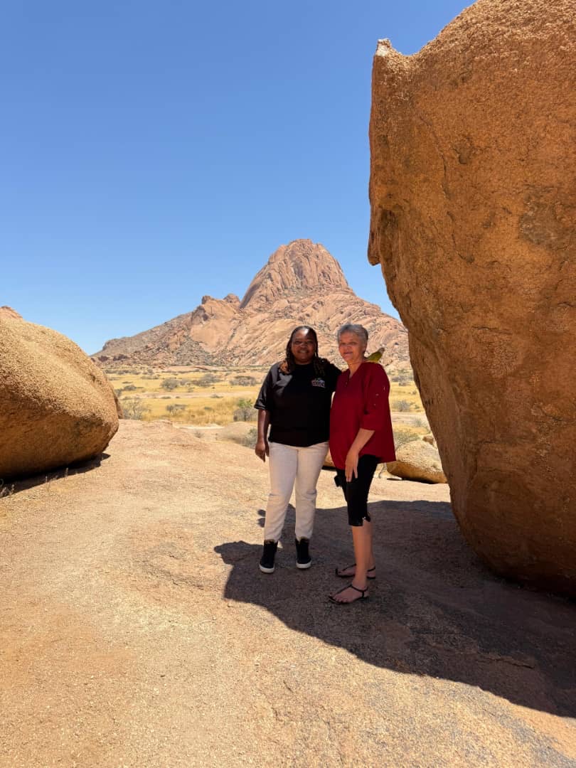 Two guests posing between massive granite boulders at Spitzkoppe with the peak in background